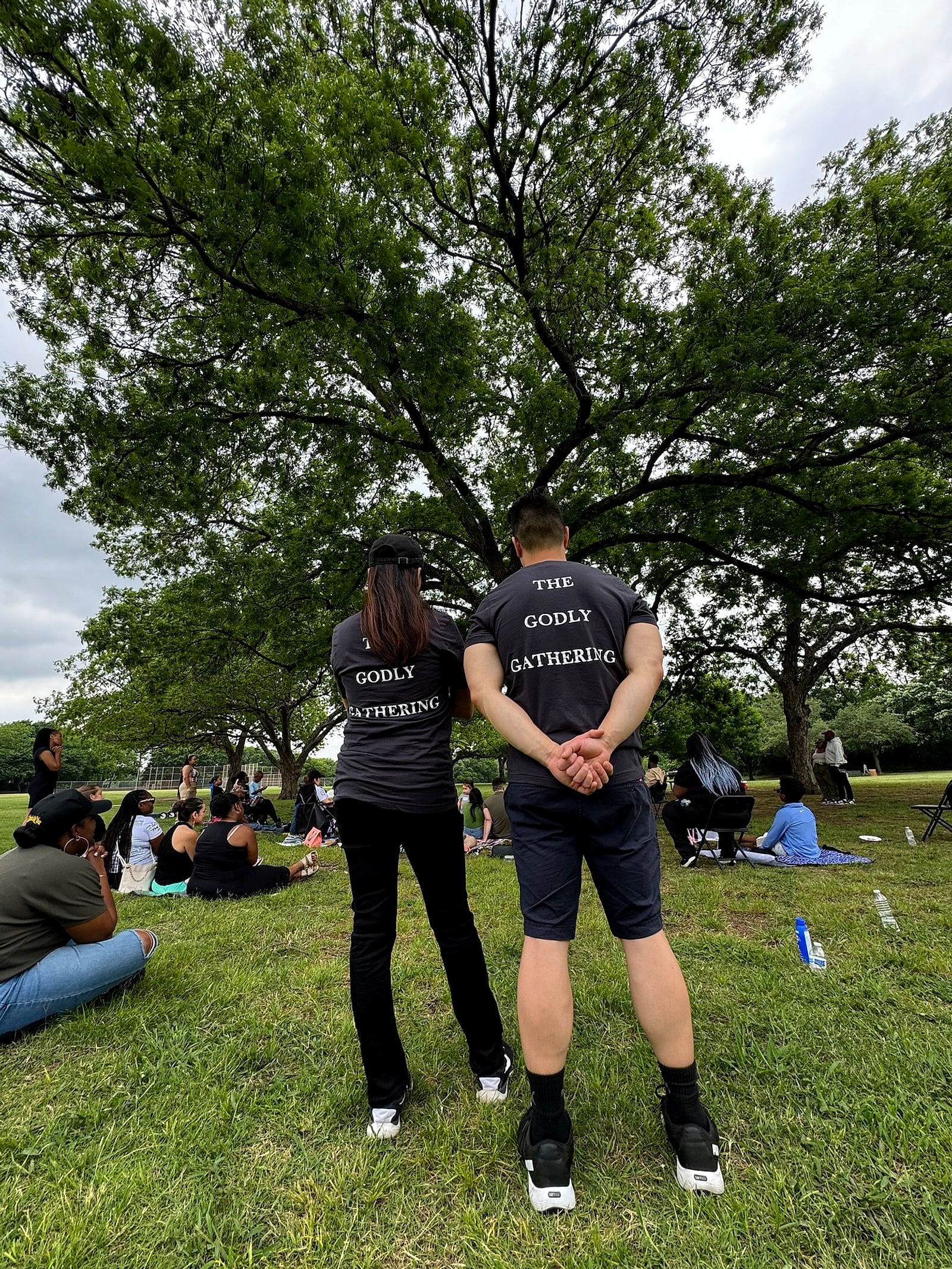 Two people in The Godly Gathering shirts under a big tree