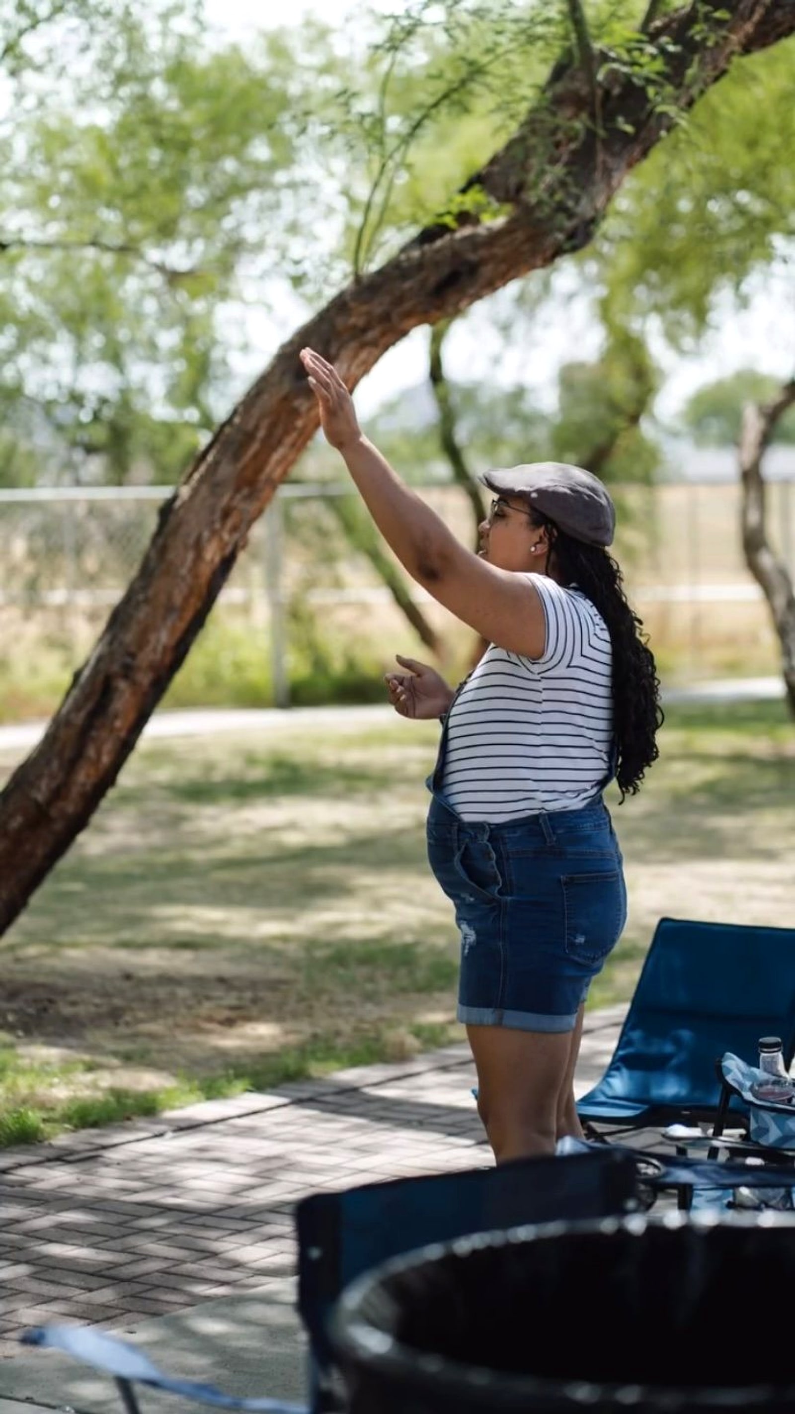 A woman with her hand raised in worship under a tree